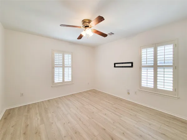 an empty room with wooden floor chandelier fan and windows
