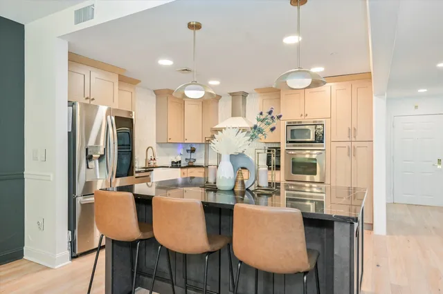 a kitchen with stainless steel appliances kitchen island granite countertop a dining table chairs refrigerator and sink
