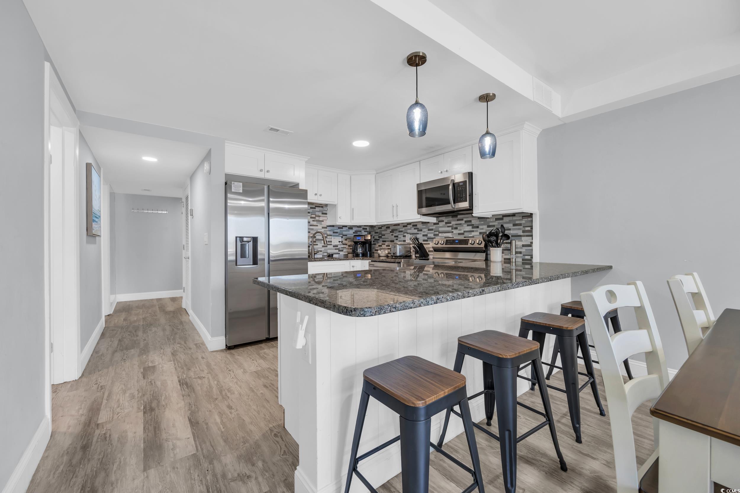 601 Mitchell Drive, Unit 203 Myrtle Beach, SC 29577 - Photo 11 of 40 Kitchen featuring a peninsula, dark stone counters, white cabinetry, appliances with stainless steel finishes, and backsplash