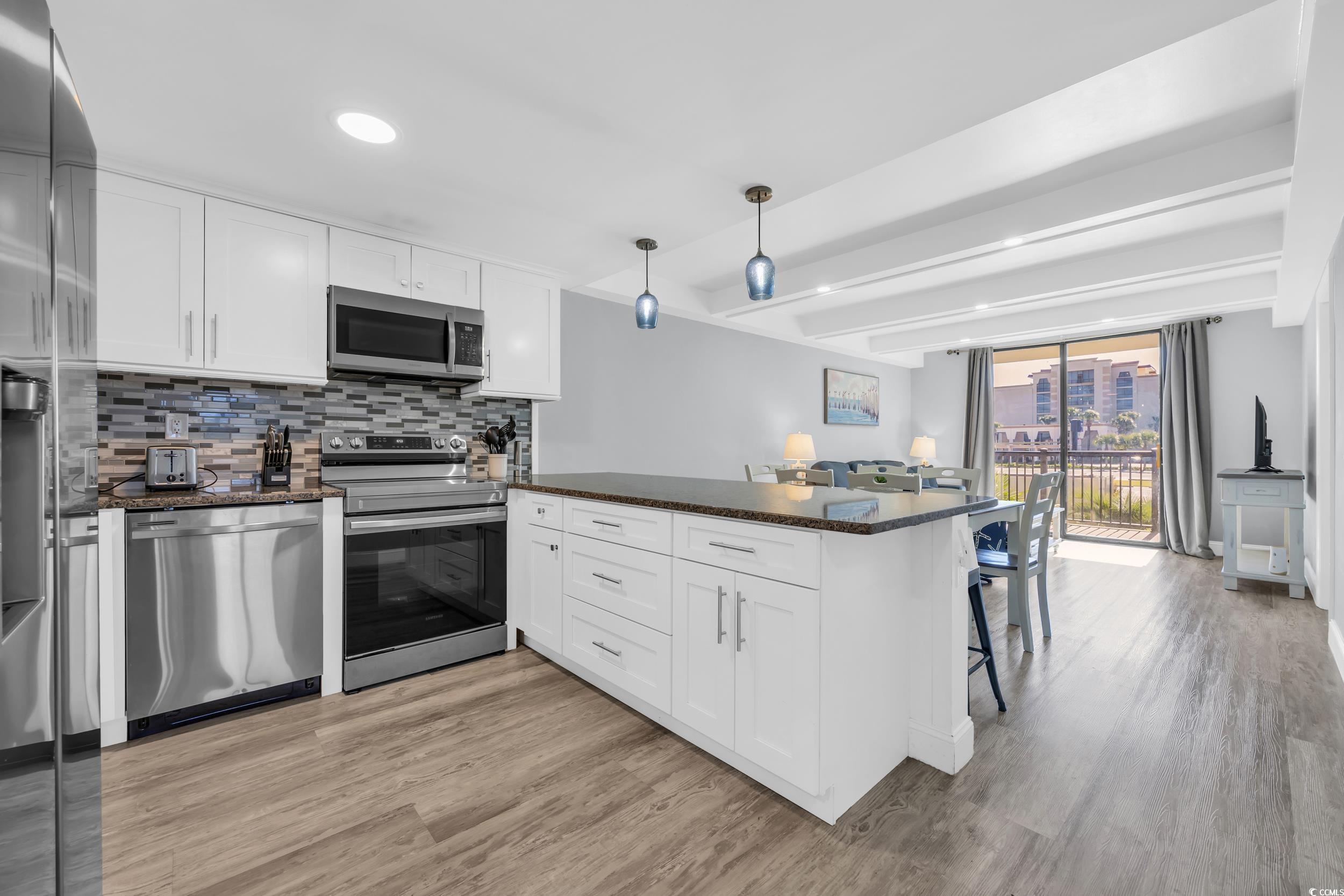 601 Mitchell Drive, Unit 203 Myrtle Beach, SC 29577 - Photo 9 of 40 Kitchen featuring white cabinets, appliances with stainless steel finishes, dark stone countertops, tasteful backsplash, and a peninsula