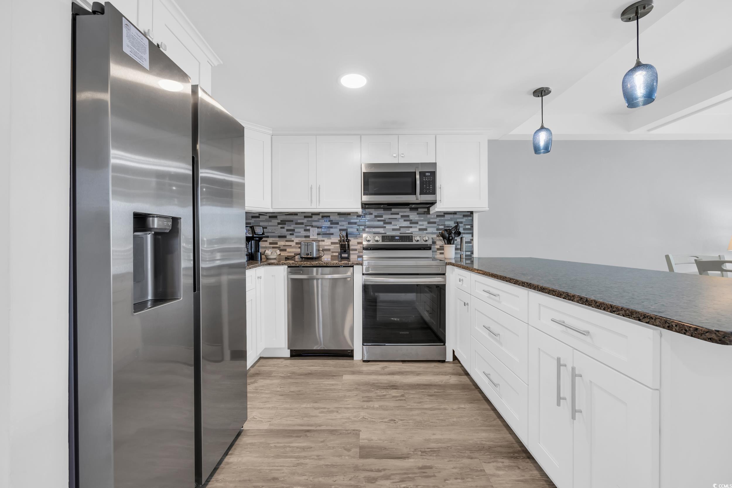 601 Mitchell Drive, Unit 203 Myrtle Beach, SC 29577 - Photo 10 of 40 Kitchen with appliances with stainless steel finishes, backsplash, white cabinetry, decorative light fixtures, and light wood-style floors