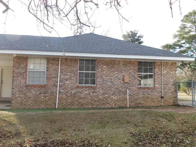 a brick house next to a yard with large trees