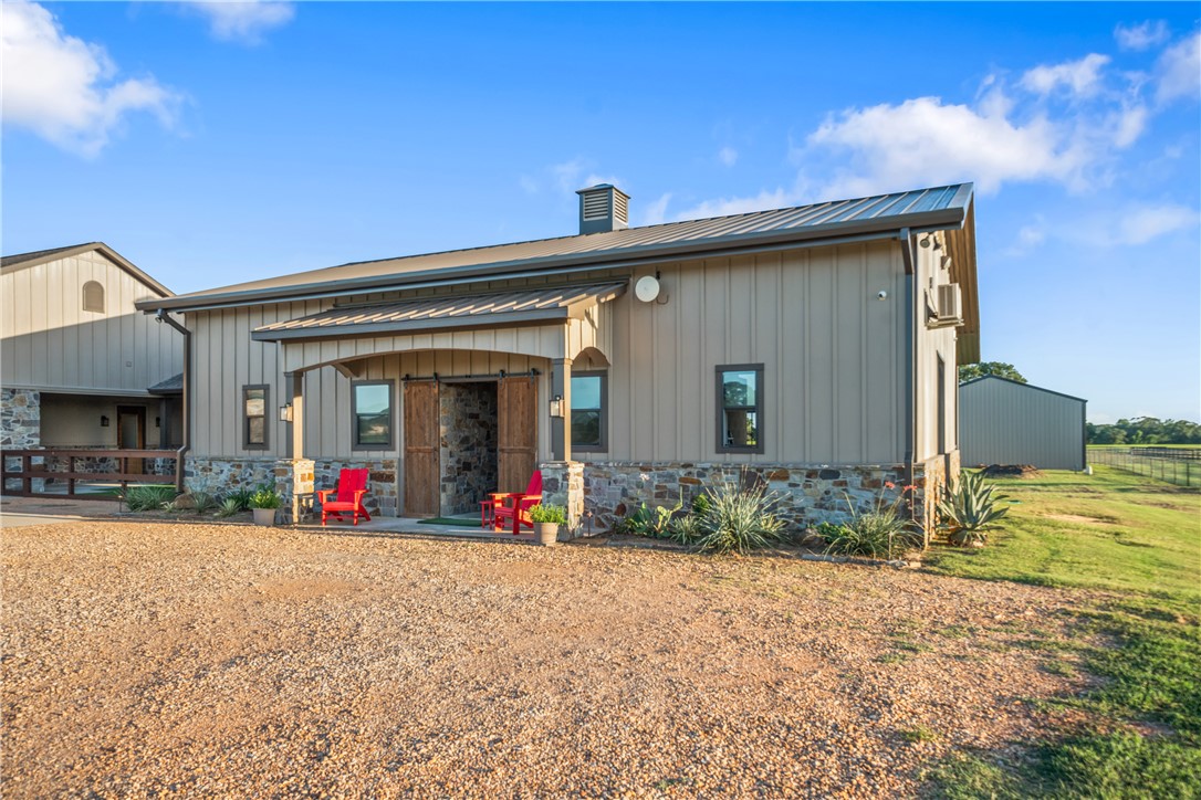30163 High Spirit Ranch Road Hempstead, TX 77445 - Photo 42 of 49 Rear view of property featuring stone siding, board and batten siding, a chimney, and a metal roof