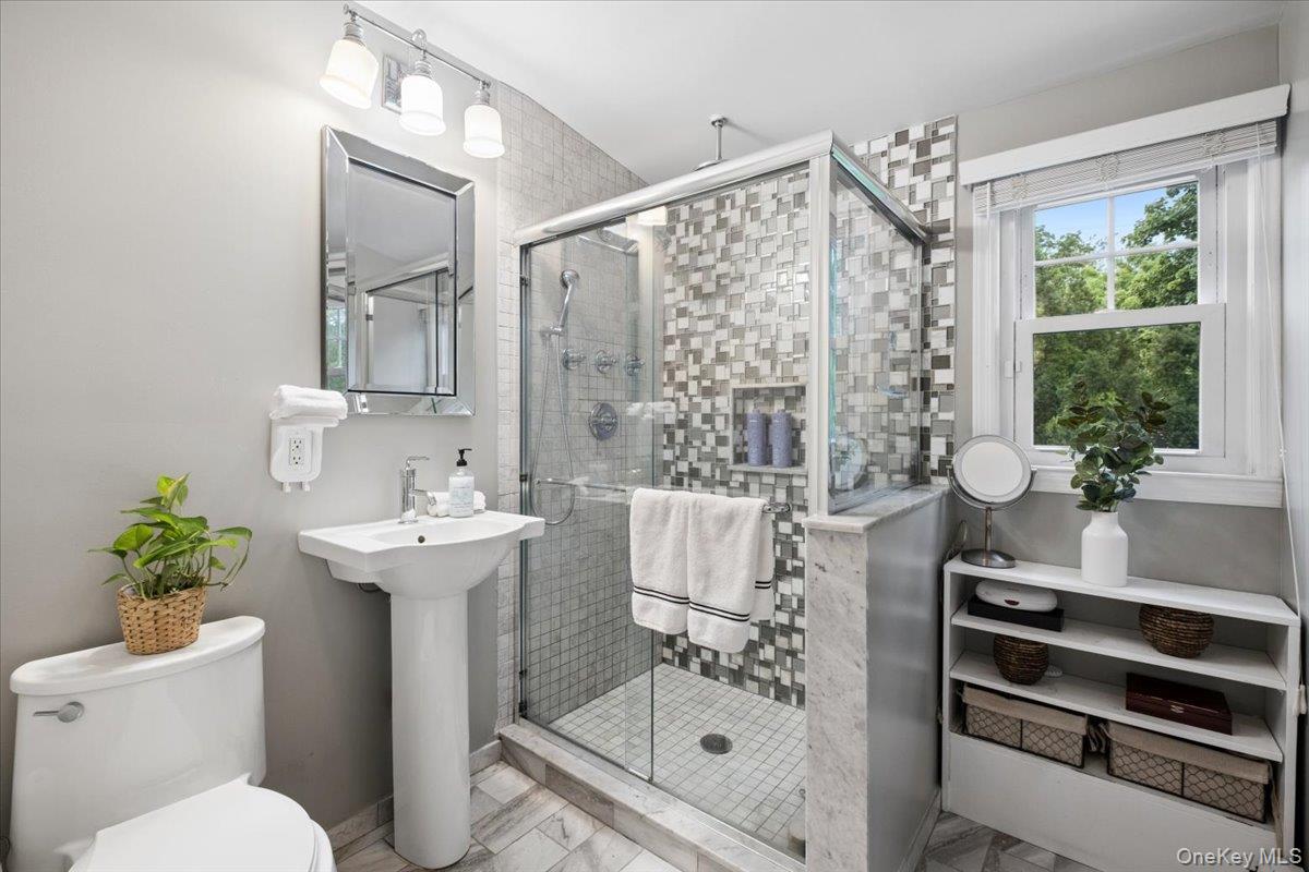 30 Stonehouse Road Scarsdale, NY 10583 - Photo 17 of 24 Glass-enclosed shower with mosaic tile surround and integrated niche, complemented by a pedestal sink, framed mirror, and track lighting.