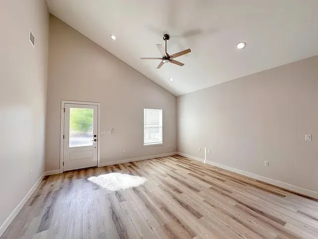 an empty room with wooden floor ceiling fan and windows