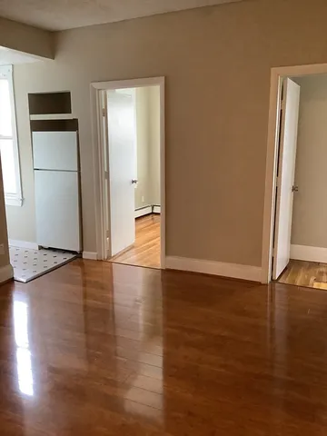 an empty room with wooden floor and a refrigerator