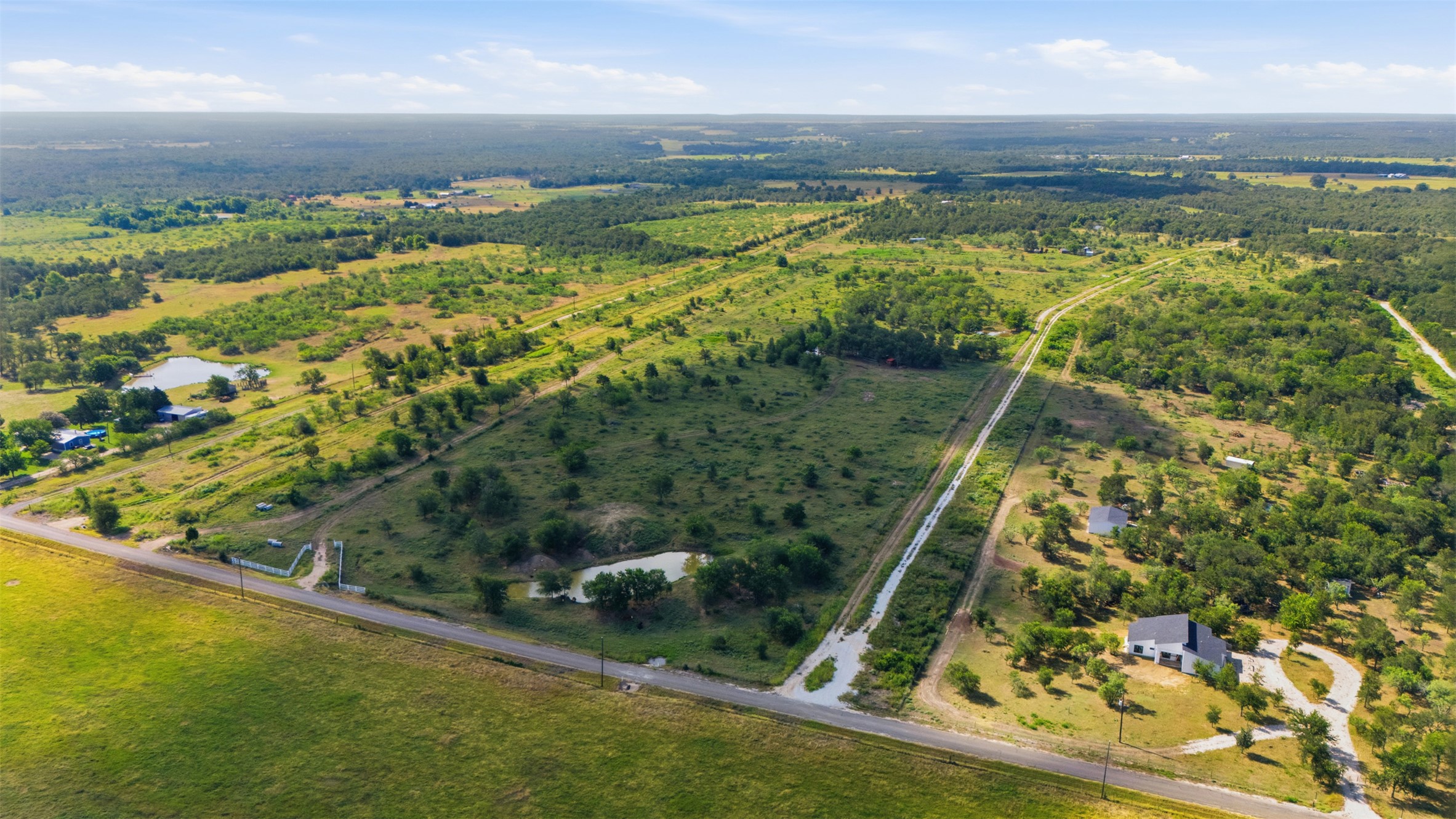 3280 County Road 466 Elgin, TX 78621 - Photo 13 of 13 An aerial panorama reveals sprawling, verdant land with a private pond and a modern residence nestled among scattered trees.