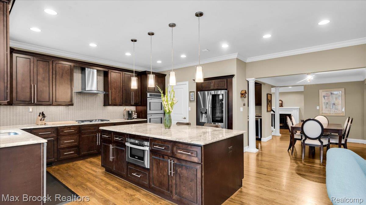 2253 Pembroke Road Birmingham, MI 48009 - Photo 15 of 56 Spacious kitchen featuring dark wood cabinetry, light-toned countertops, a central island with pendant lighting, a stainless steel range hood, and double wall ovens