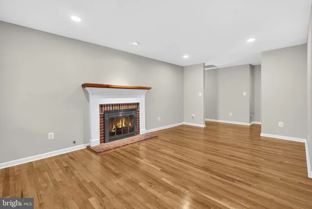 a view of an empty room with wooden floor fireplace and a window