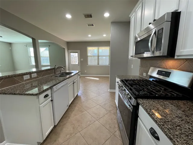a kitchen with granite countertop a sink a counter top space stainless steel appliances and cabinets