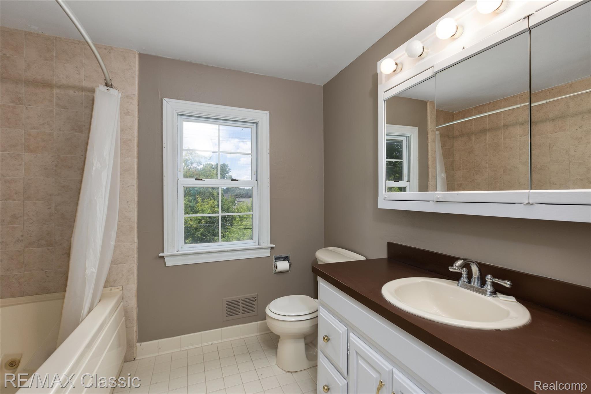 4268 Covered Bridge Road Bloomfield Hills, MI 48302 - Photo 22 of 35 Full bathroom featuring a window, tile flooring, a tub-shower combination with tile surround, a vanity with an integrated sink and dark countertop, and a mirrored medicine cabinet with integrated lighting
