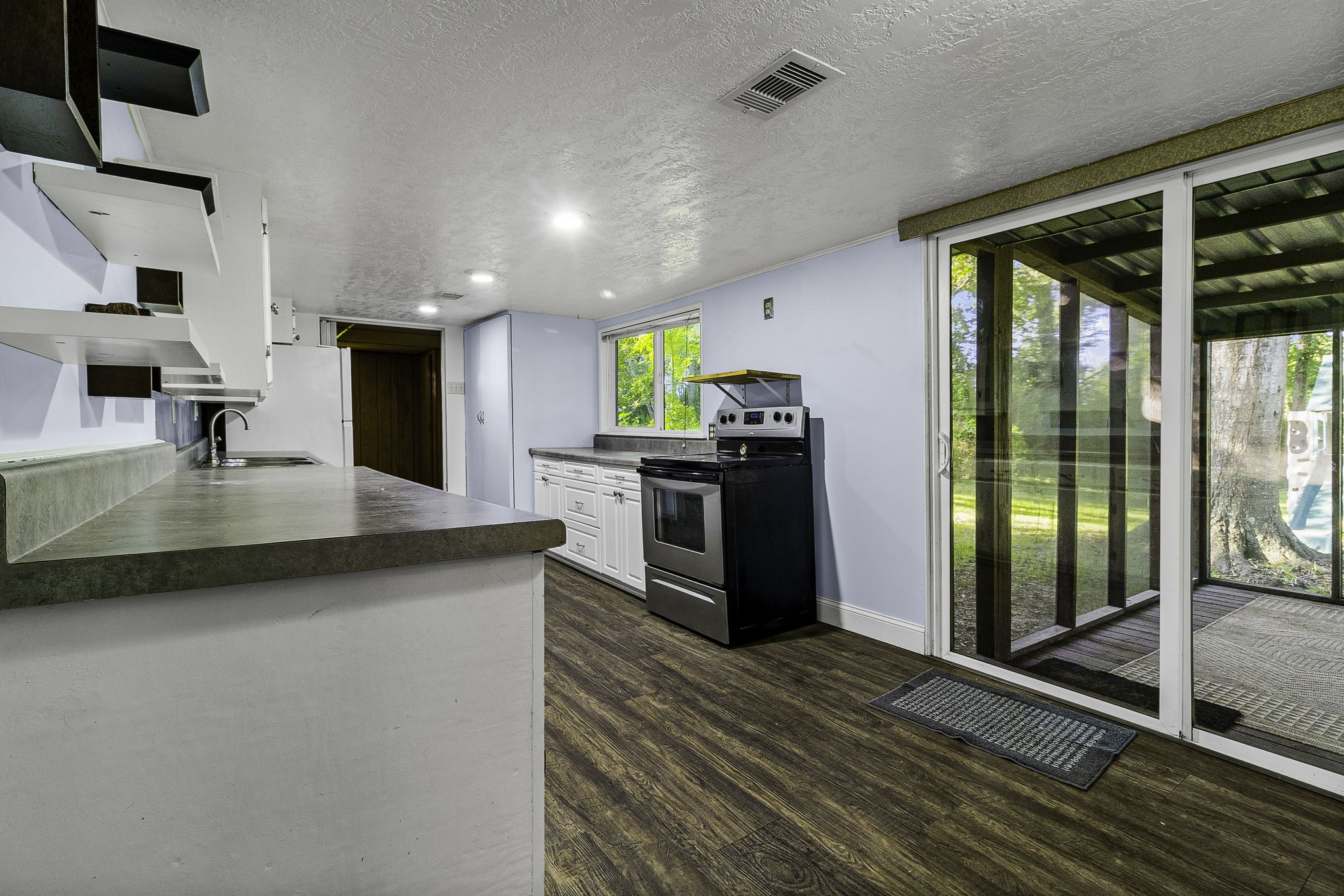 450 River Road Goodrich, TX 77335 - Photo 11 of 40 Bright kitchen with modern open shelving, sleek countertops, and stainless steel appliances. Sliding glass doors lead to a serene outdoor space, enhancing the open feel.
