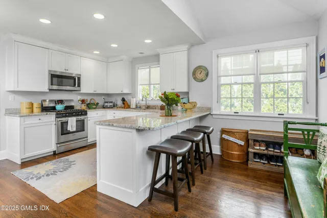 a kitchen with stainless steel appliances granite countertop wooden floor a stove a sink a refrigerator cabinets and dining table