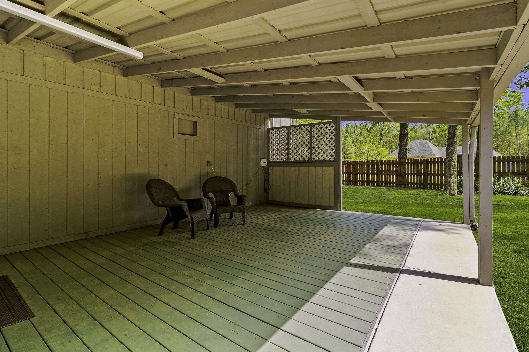 21 Red Oak Circle Point Blank, TX 77364 - Photo 23 of 32 Covered patio with a wooden deck, featuring two chairs and a view of a fenced backyard with lush grass and trees. Ideal for outdoor relaxation and entertaining.