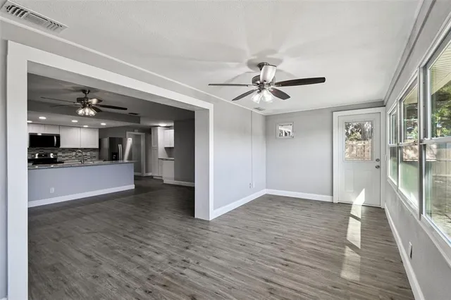 an empty room with wooden floor chandelier fan and windows