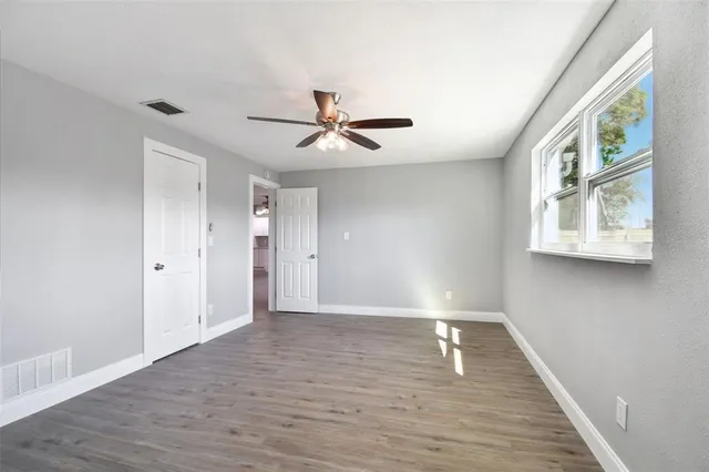a view of an empty room with wooden floor and a ceiling fan
