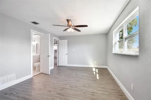 an empty room with wooden floor ceiling fan and windows
