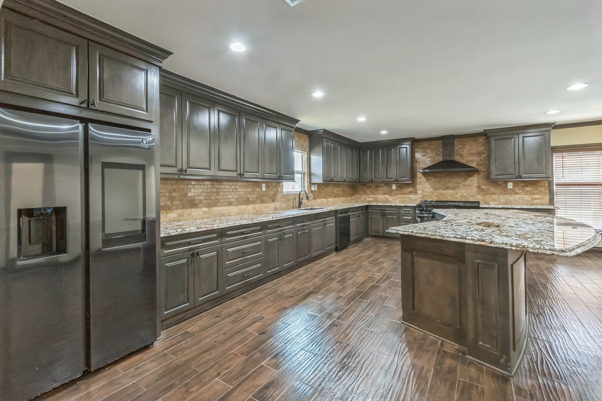 24578 Derry Street Hempstead, TX 77445 - Photo 12 of 50 Dream kitchen features dark wood cabinets, granite countertops, and a large island. It has a modern refrigerator, ample storage, and recessed lighting, complemented by a warm, wood-look tile floor.