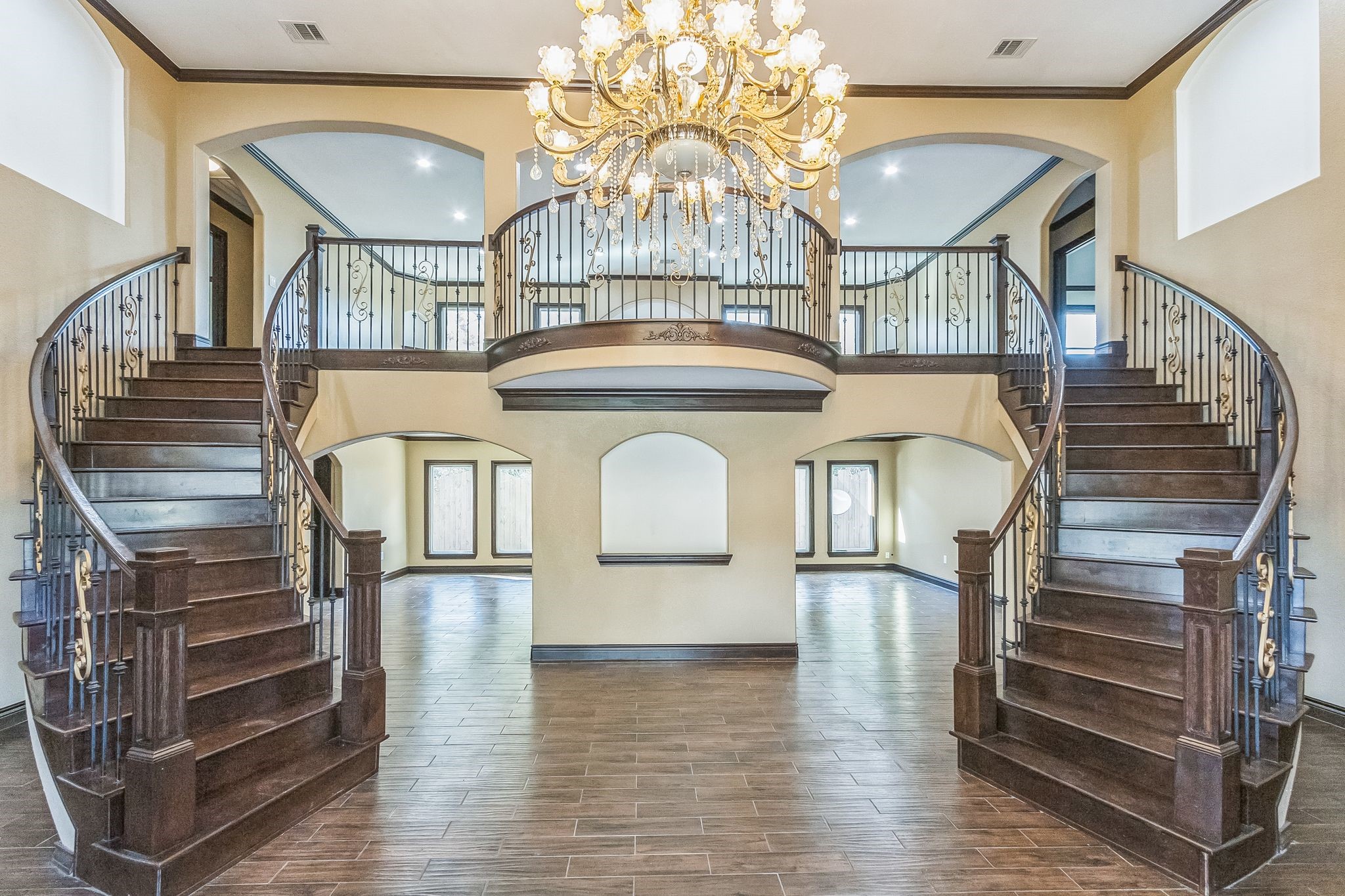 24578 Derry Street Hempstead, TX 77445 - Photo 4 of 50 This grand foyer features a stunning double staircase with dark wood and elegant wrought-iron railings. A large, ornate chandelier adds a touch of luxury, while arched doorways and high ceilings enhance the spacious, open feel of the area.