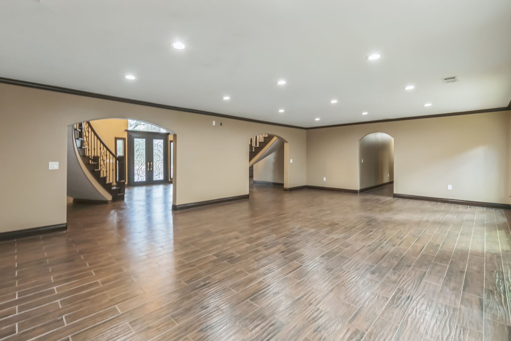 24578 Derry Street Hempstead, TX 77445 - Photo 6 of 50 This spacious interior features polished wood-look flooring, recessed lighting, and archways leading to a grand staircase and entryway, creating an elegant and open ambiance.
