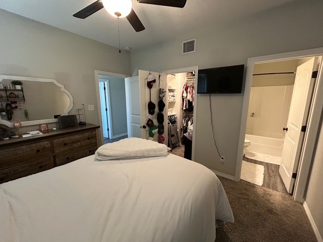 6942 Halter Loop College Station, TX 77845 - Photo 12 of 28 Bedroom featuring a walk in closet, dark carpet, ceiling fan, and connected bathroom