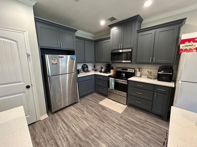6942 Halter Loop College Station, TX 77845 - Photo 7 of 28 Kitchen featuring stainless steel appliances, backsplash, light wood-style flooring, light stone counters, and ornamental molding