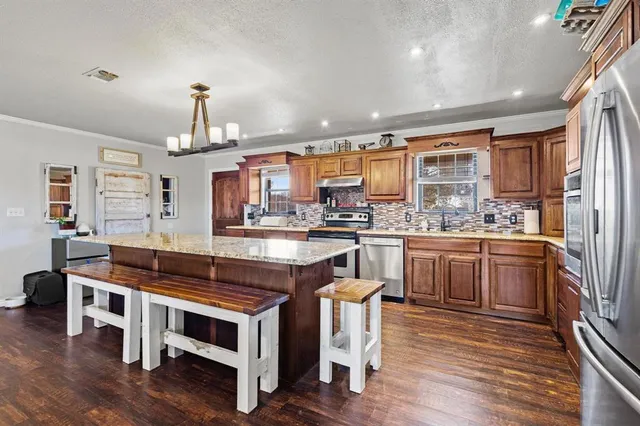 a kitchen with stainless steel appliances granite countertop a stove a sink dishwasher and a refrigerator with wooden floor