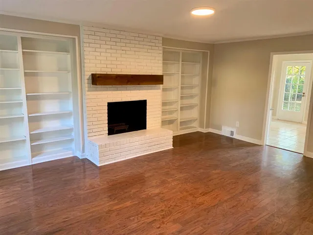 an empty room with wooden floor fireplace and windows