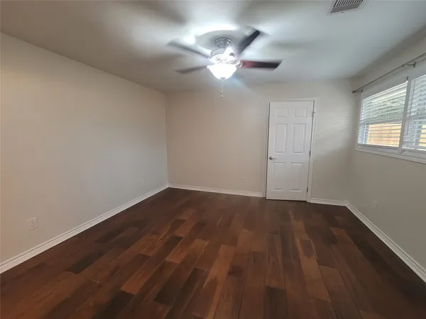 a view of an empty room with wooden floor and a fan