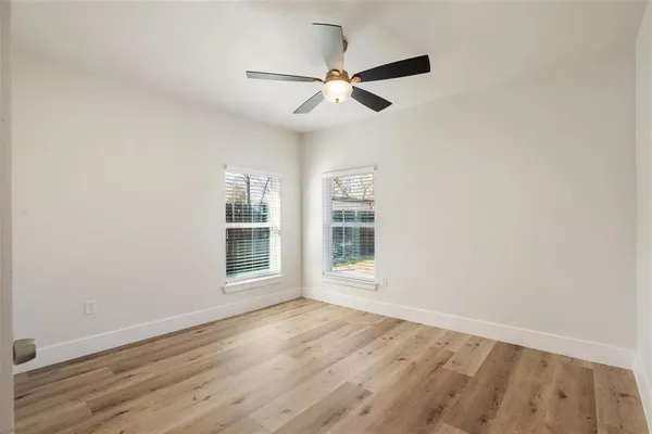 an empty room with wooden floor fan and windows