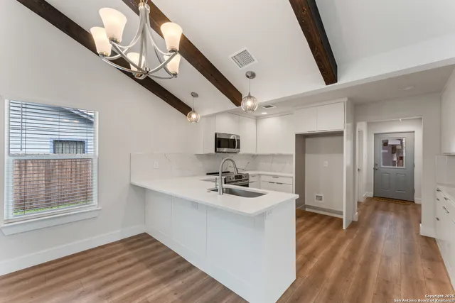 a view of an empty room with wooden floor and a chandelier fan