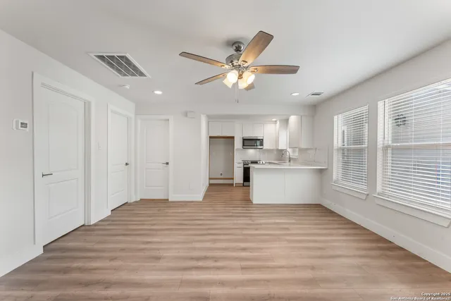 an empty room with wooden floor fan and windows