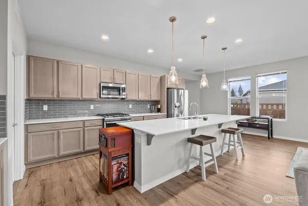 a kitchen with stainless steel appliances granite countertop a stove top oven a sink a refrigerator white cabinets and wooden floor