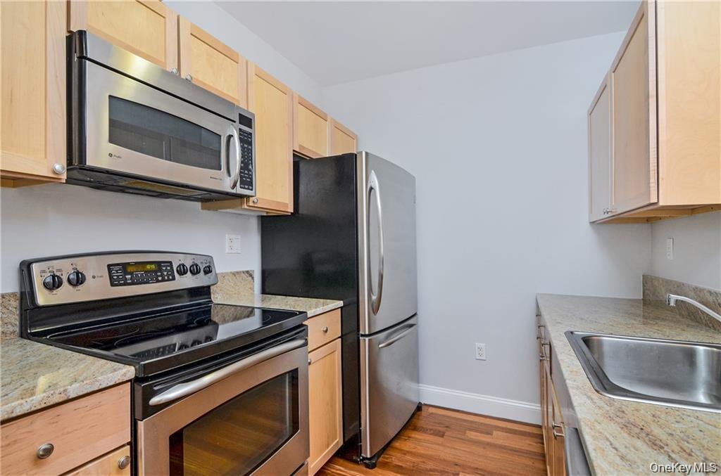 543 Main Street, Unit 402 New Rochelle, NY 10801 - Photo 6 of 21 Kitchen with stainless steel appliances, light brown cabinetry, light wood-style floors, and light stone countertops
