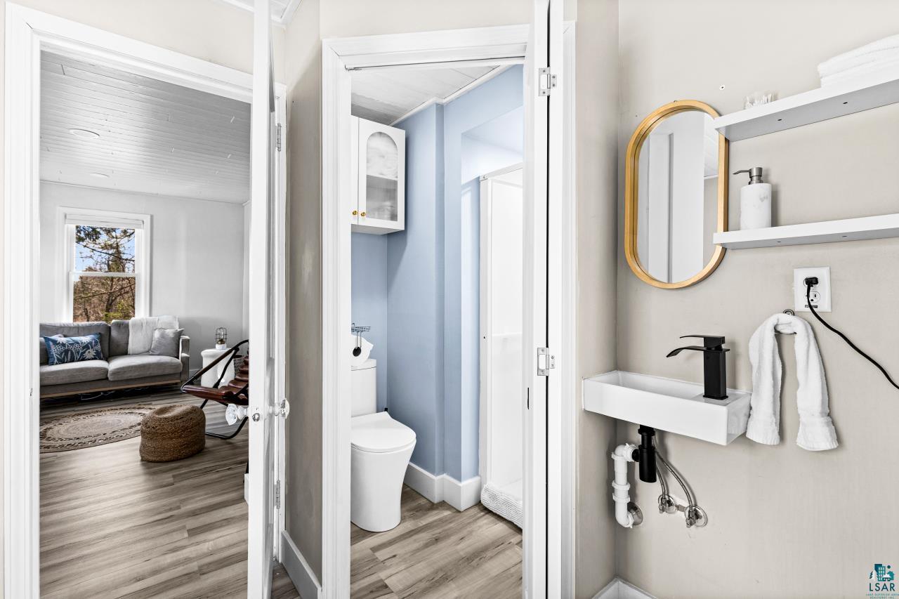 3645 Haines Road Hermantown, MN 55811 - Photo 22 of 35 Compact bathroom featuring a modern wall-mounted sink with a matte black faucet, a gold-framed oval mirror, and white floating shelves