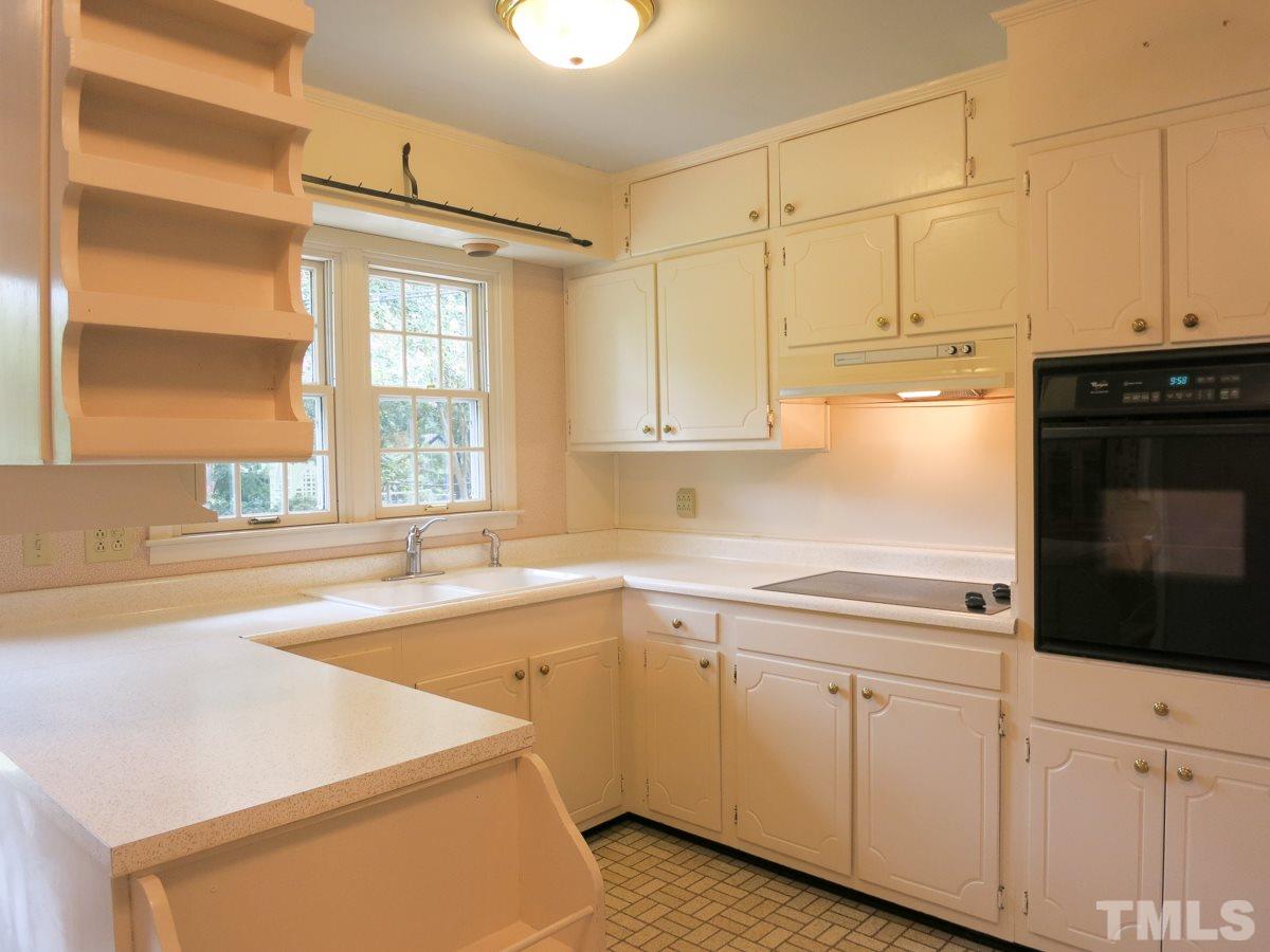 4701 Latimer Road Raleigh, NC 27609 - Photo 7 of 25 The eat-in Kitchen features a vinyl flr, white cabinets, neutral laminate ctrs, glass cooktop, wall oven, range hood, DW, deep dbl bowl sink w/newer brushed nickel faucet & door to the backyard.