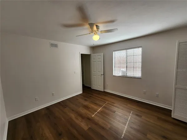 an empty room with wooden floor ceiling fan and windows