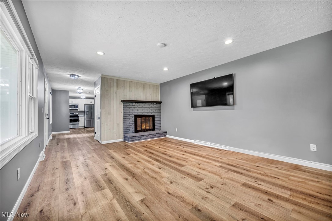 5306 Lockwood Road Madison, OH 44057 - Photo 5 of 28 Unfurnished living room featuring a textured ceiling, light wood-type flooring, and a fireplace