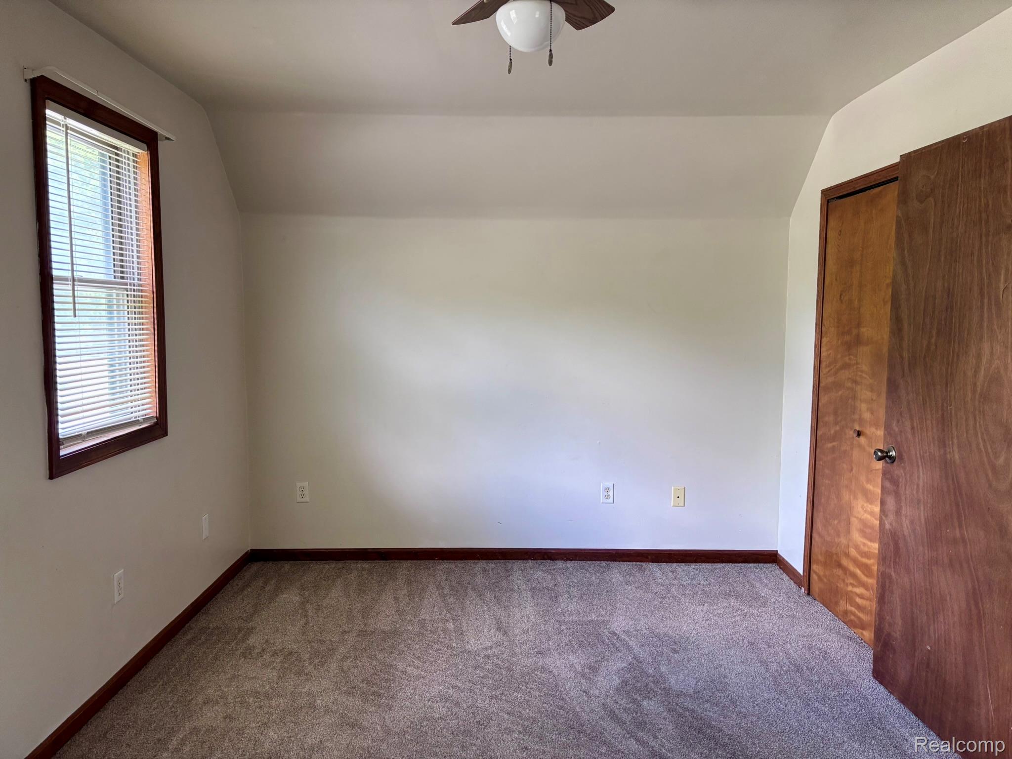 Neutral wall tones with sloped ceiling, wood-trim window with blinds, carpeted flooring, and a wood-finish closet door