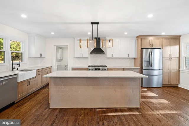 a large kitchen with stainless steel appliances a refrigerator a sink dishwasher a stove and white cabinets with wooden floor