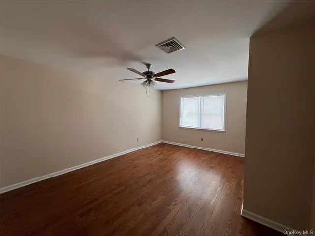 an empty room with wooden floor chandelier fan and windows