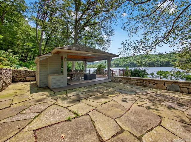 a view of a patio with table and chairs under an umbrella with large trees