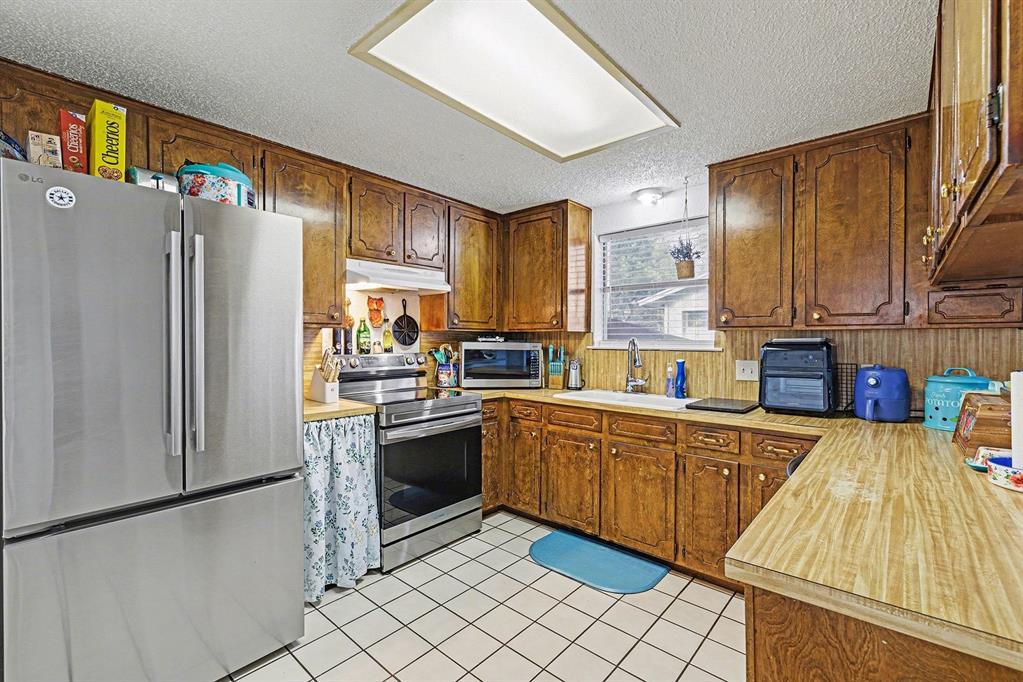 6013 Robin Drive Watauga, TX 76148 - Photo 13 of 30 Kitchen with stainless steel appliances, light countertops, a textured ceiling, wood finish cabinetry, and light tile patterned floors