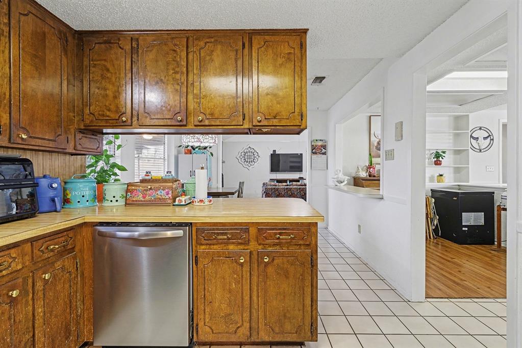 6013 Robin Drive Watauga, TX 76148 - Photo 14 of 30 Kitchen with stainless steel dishwasher, a peninsula, a textured ceiling, light countertops, and light tile patterned floors