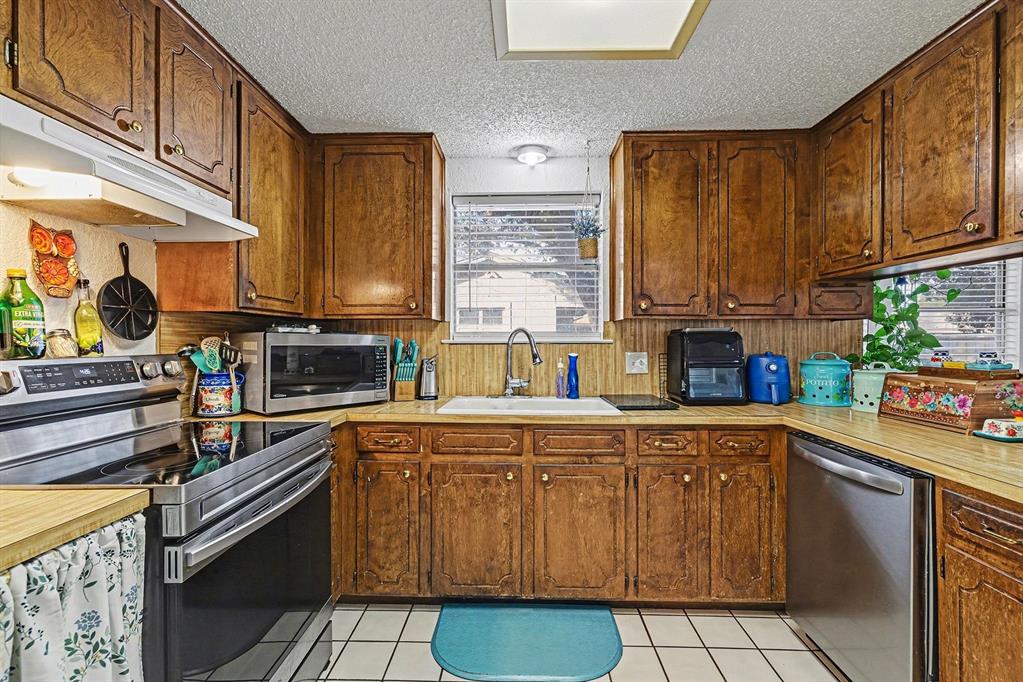 6013 Robin Drive Watauga, TX 76148 - Photo 15 of 30 Kitchen featuring stainless steel appliances, light countertops, a textured ceiling, light tile patterned floors, and wood finish cabinetry