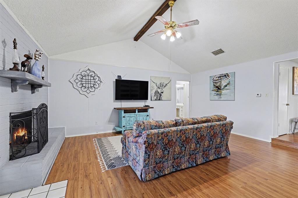 6013 Robin Drive Watauga, TX 76148 - Photo 18 of 30 Living room featuring beam ceiling, a textured ceiling, wood finished floors, a ceiling fan, and a brick fireplace