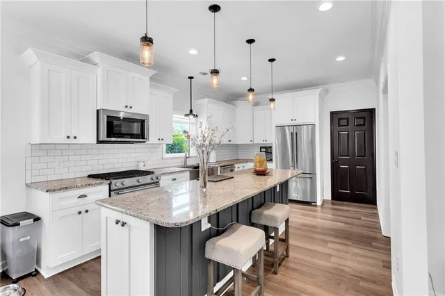 a kitchen with kitchen island granite countertop a stove a sink a refrigerator and white cabinets with wooden floor