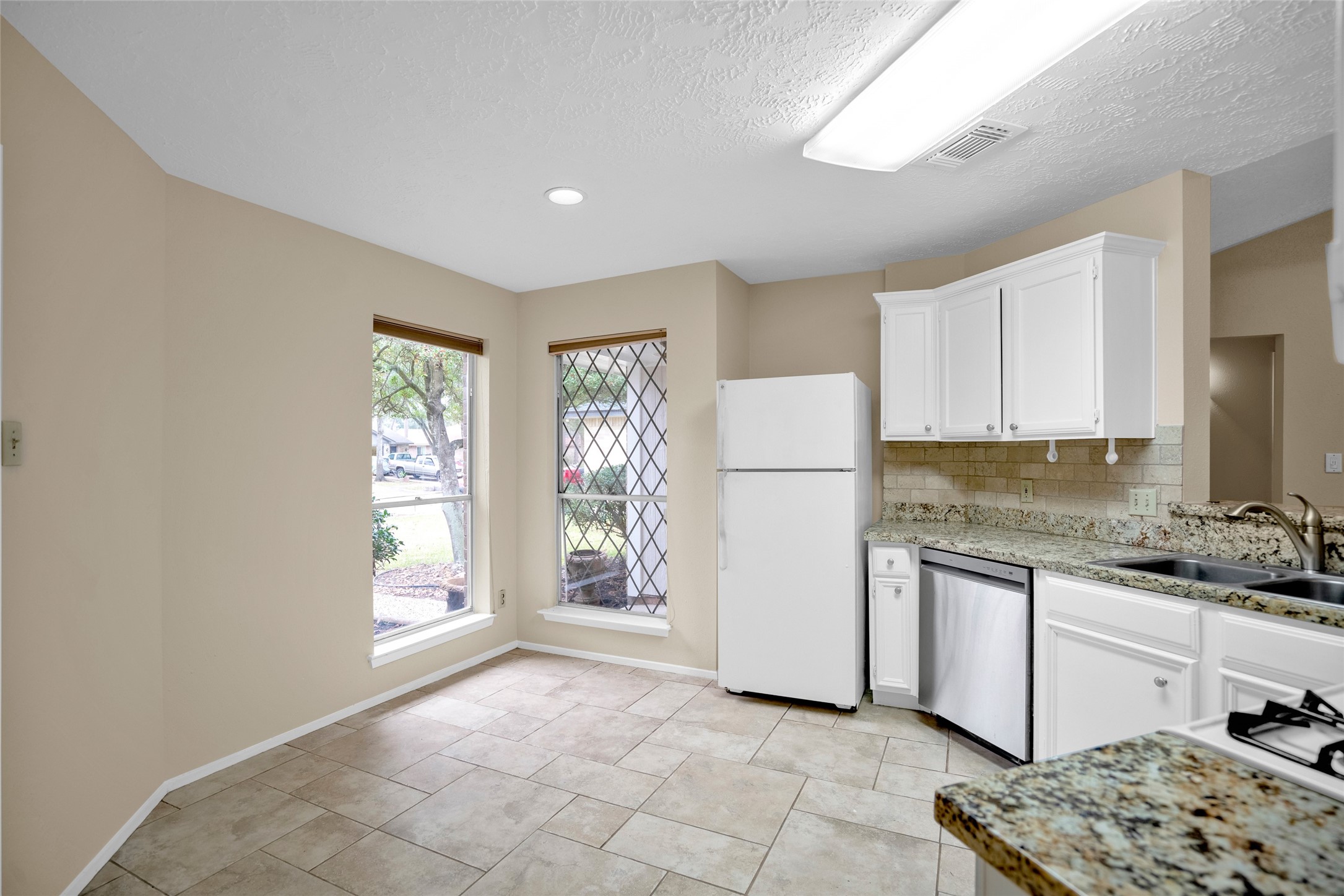 17323 Northchapel Street Spring, TX 77379 - Photo 13 of 37 Kitchen with granite countertops, white cabinetry, and natural light from multiple windows.