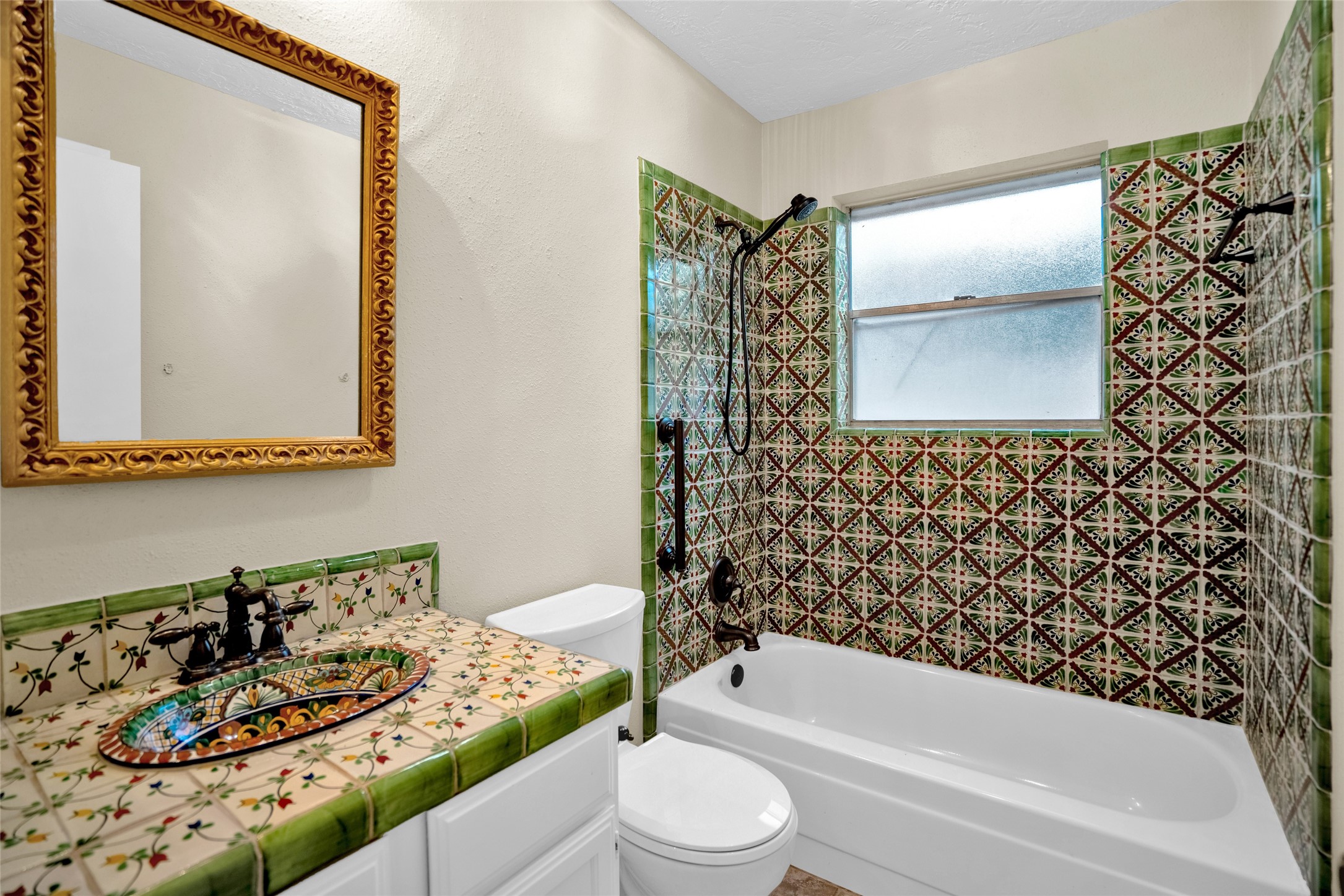 17323 Northchapel Street Spring, TX 77379 - Photo 21 of 37 Charming secondary bathroom showcasing beautiful Mediterranean-inspired tilework, custom vanity, and a tub/shower combination. Warm tones and intricate detailing create a unique, character-filled space that feels both timeless and inviting.