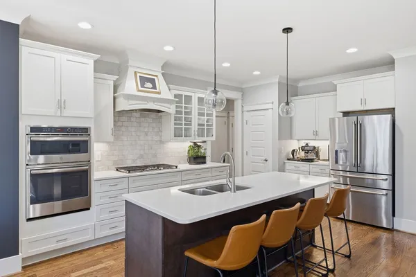 a kitchen with stainless steel appliances a stove a sink a refrigerator and chairs